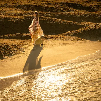 晴れた砂浜で、笑顔で子供を背負って楽しそうに過ごす女性。