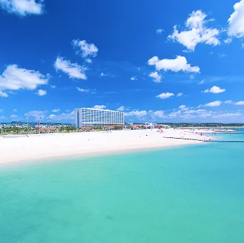 透き通ったエメラルドグリーンの海と白い砂浜、その奥に建つ白いホテルの外観。