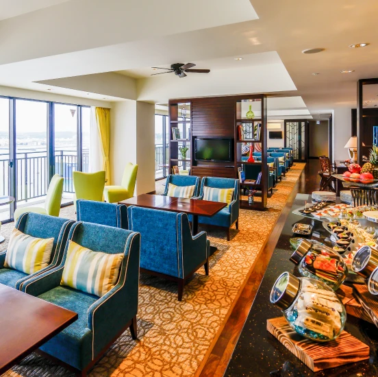 ゆったりとしたソファに座ってくつろぐ女性客へ、スタッフが笑顔で飲み物を提供している様子。落ち着いた照明の中、きめ細やかなサービスが行われているラウンジのワンシーンです。