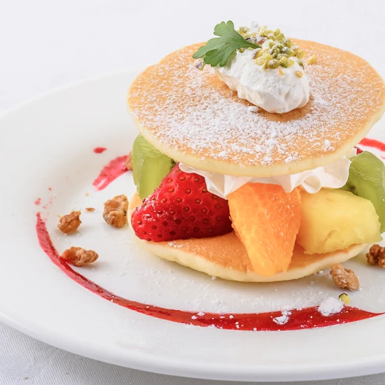 イチゴやキウイなどのフルーツと生クリームが贅沢に盛り付けられた、色鮮やかなパンケーキ風スイーツ。
