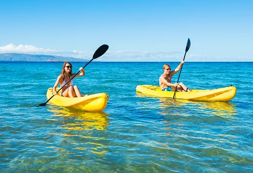 快晴の美々ビーチいとまんで、二人の男女がそれぞれ黄色のカヤックを漕いでマリンアクティビティを楽しんでいる様子。